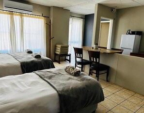 Habitación de hotel con dos camas, un escritorio con sillas, un refrigerador y una ventana con cortinas.