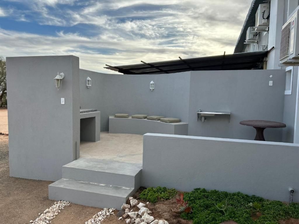Un patio extérieur moderne avec un banc en béton, une petite table et un luminaire fixé au mur.