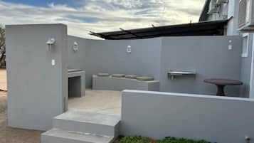 Un patio extérieur moderne avec un banc en béton, une petite table et un luminaire fixé au mur.