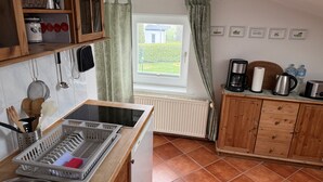 Eine Küche mit Einbauherd, einem Fenster mit Vorhängen, einem Heizkörper und einem Holzkasten mit Schubladen.