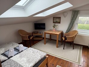 Una stanza in stile loft con un velux, una televisione, un tavolino con un vaso, due poltrone in vimini, un divano e vista sul verde.