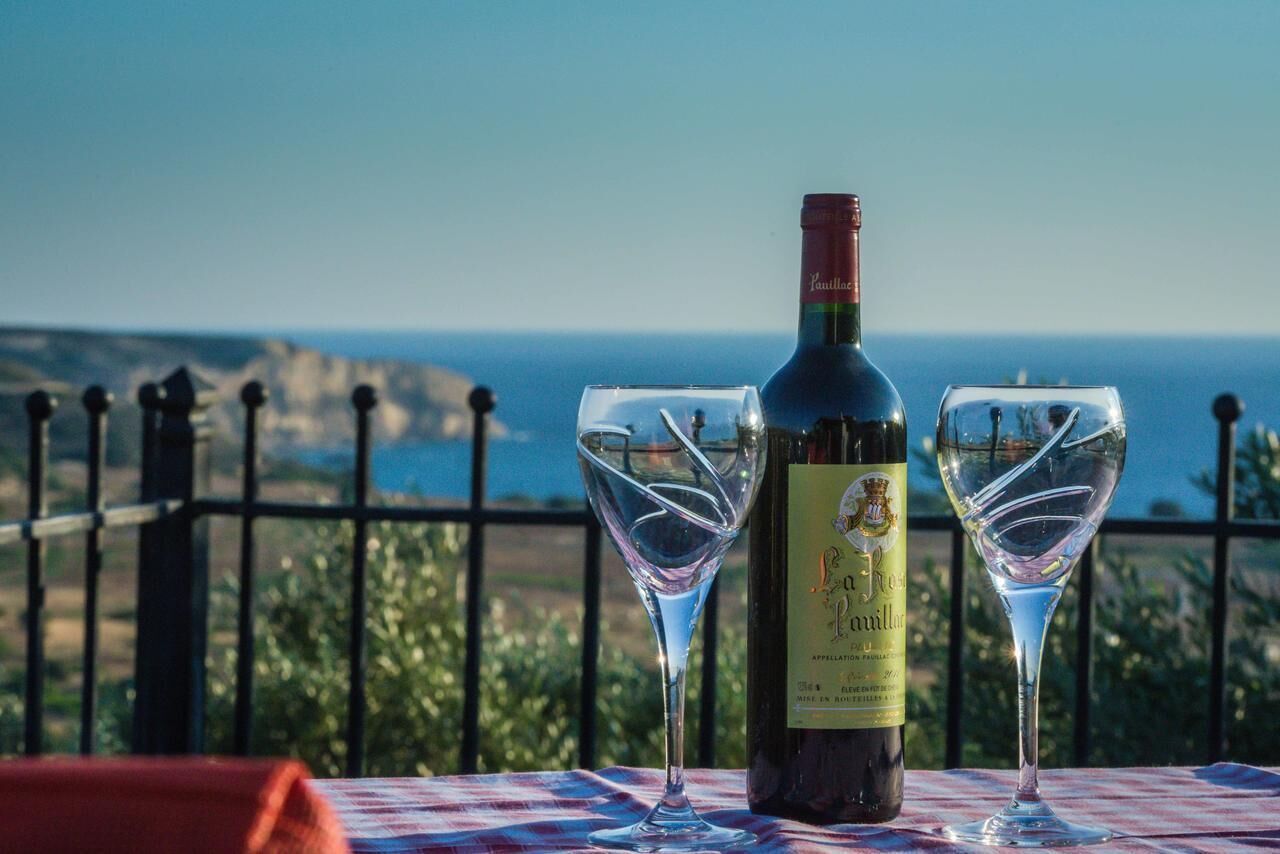 A bottle of wine and two glasses on a table with a view of the sea.