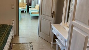 A room with a bed, a dresser, and a door leading to a living area with a sofa and curtains. - Villa Georgia (Faistos)