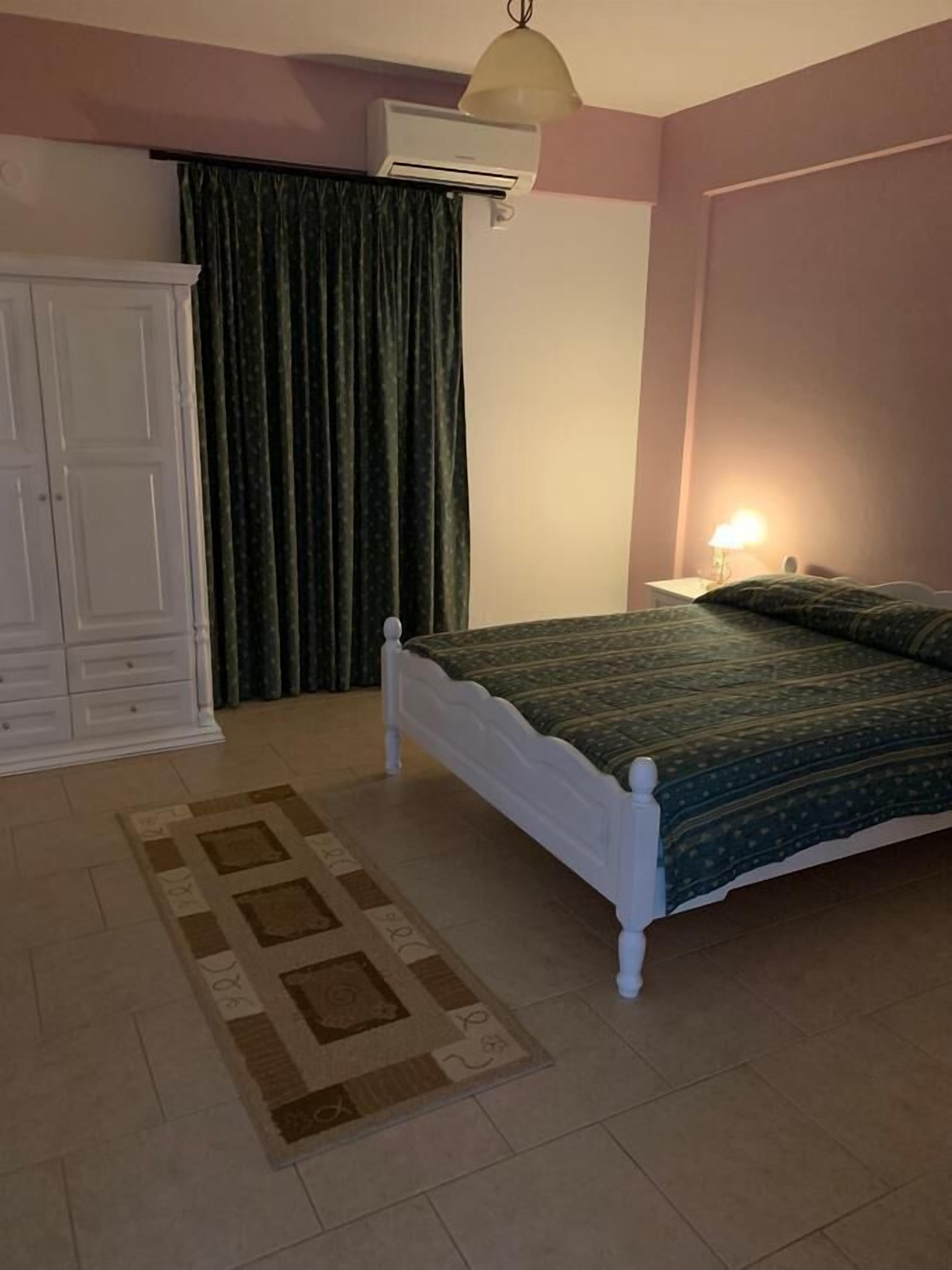 Ein Schlafzimmer mit Bett, Kleiderschrank, Klimaanlage, Lampe und einem gemusterten Teppich.