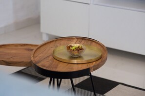 A round wooden table with a glass top and a bowl of fruit.