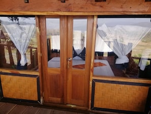 A wooden cabin with a sliding glass door, two windows with white curtains, and a wooden floor.