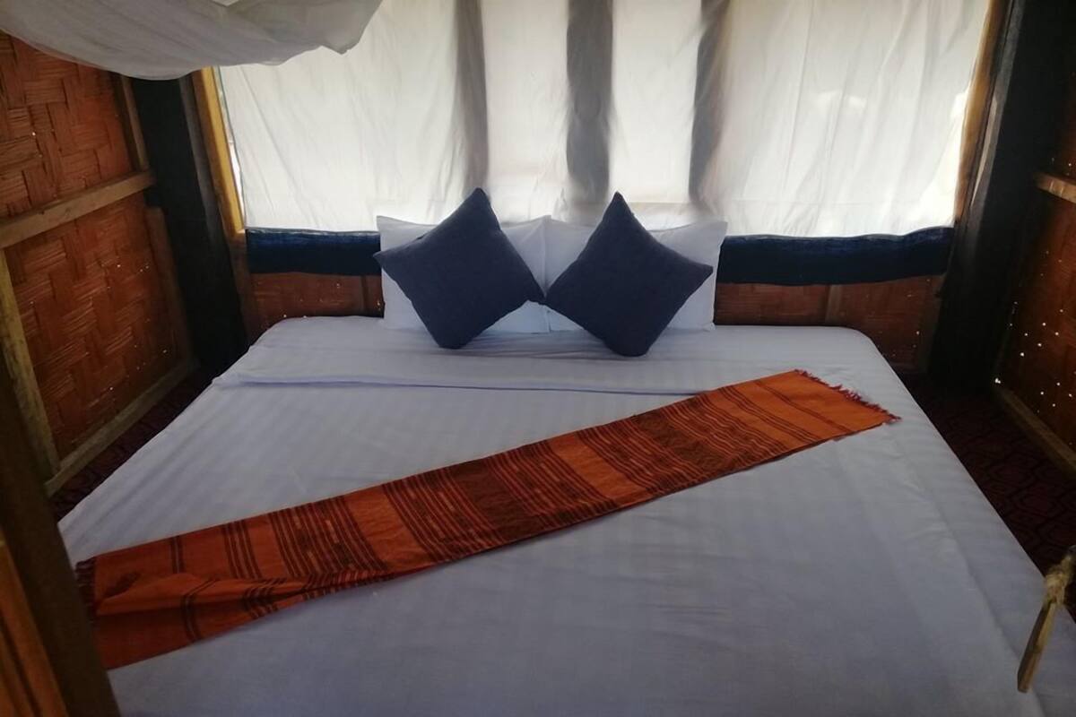 A bed with white bedding, two dark pillows, and a red patterned throw.