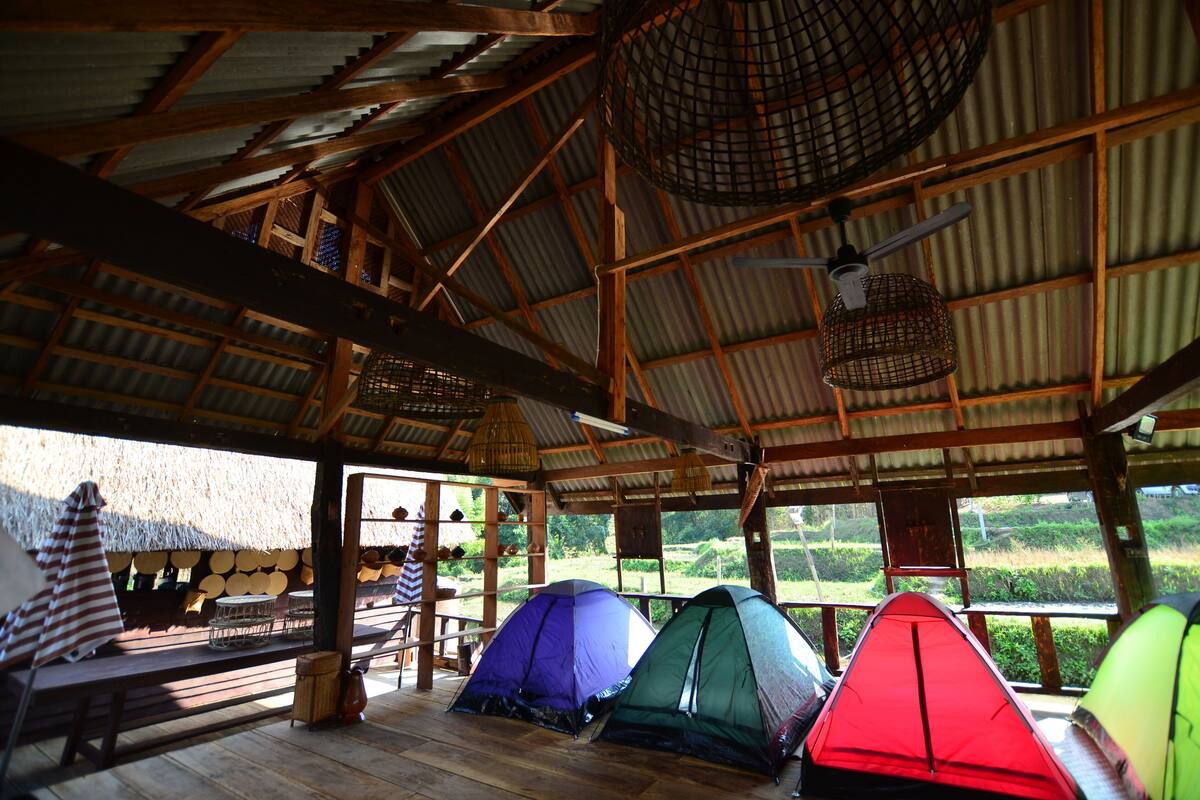 A rustic wooden structure with a thatched roof, multiple tents, and a view of a lush landscape.
