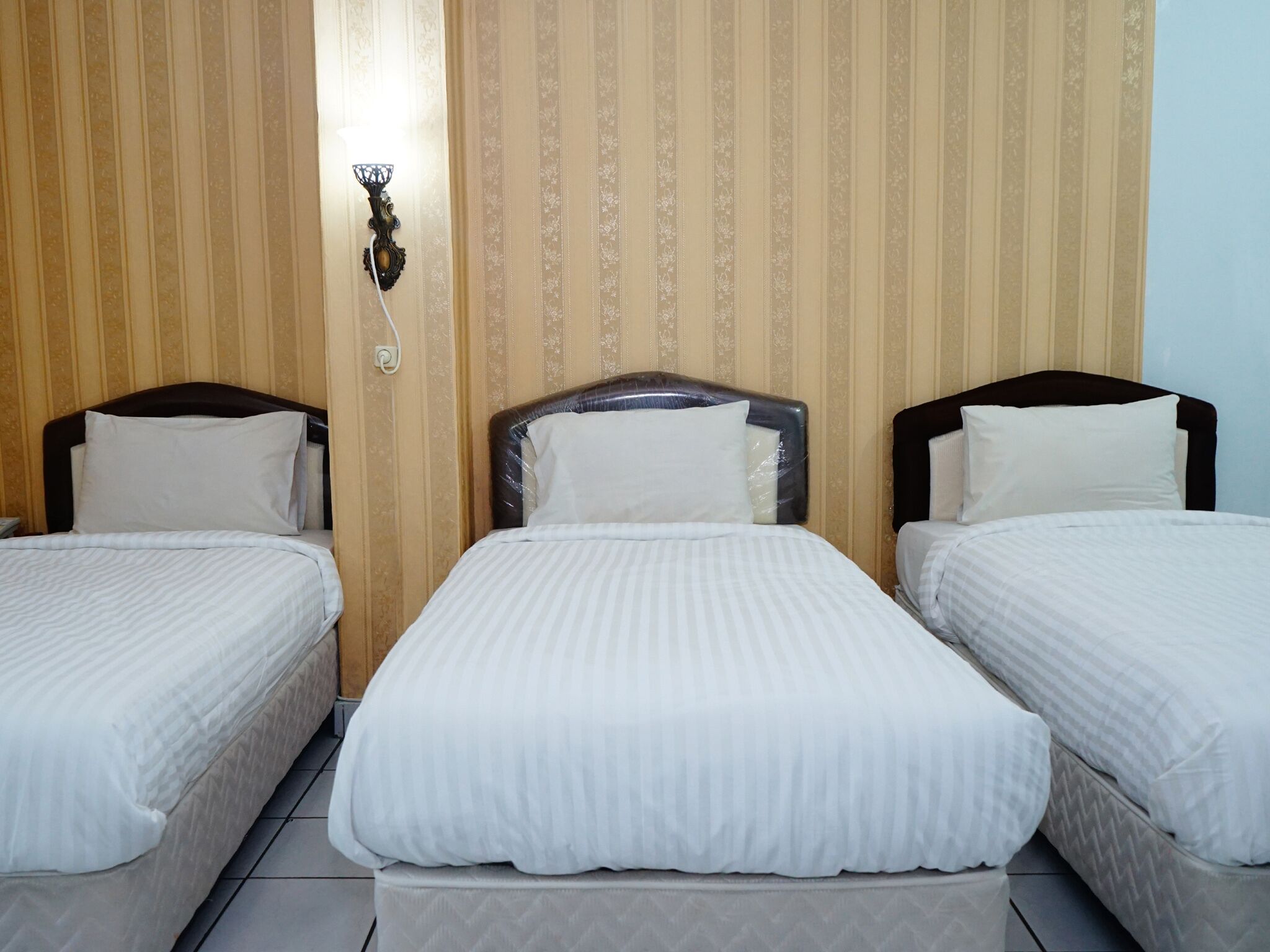 Una habitación de hotel con tres camas individuales, cada una con cabecero y ropa de cama blanca.