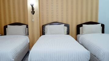 Una habitación de hotel con tres camas individuales, cada una con cabecero y ropa de cama blanca.
