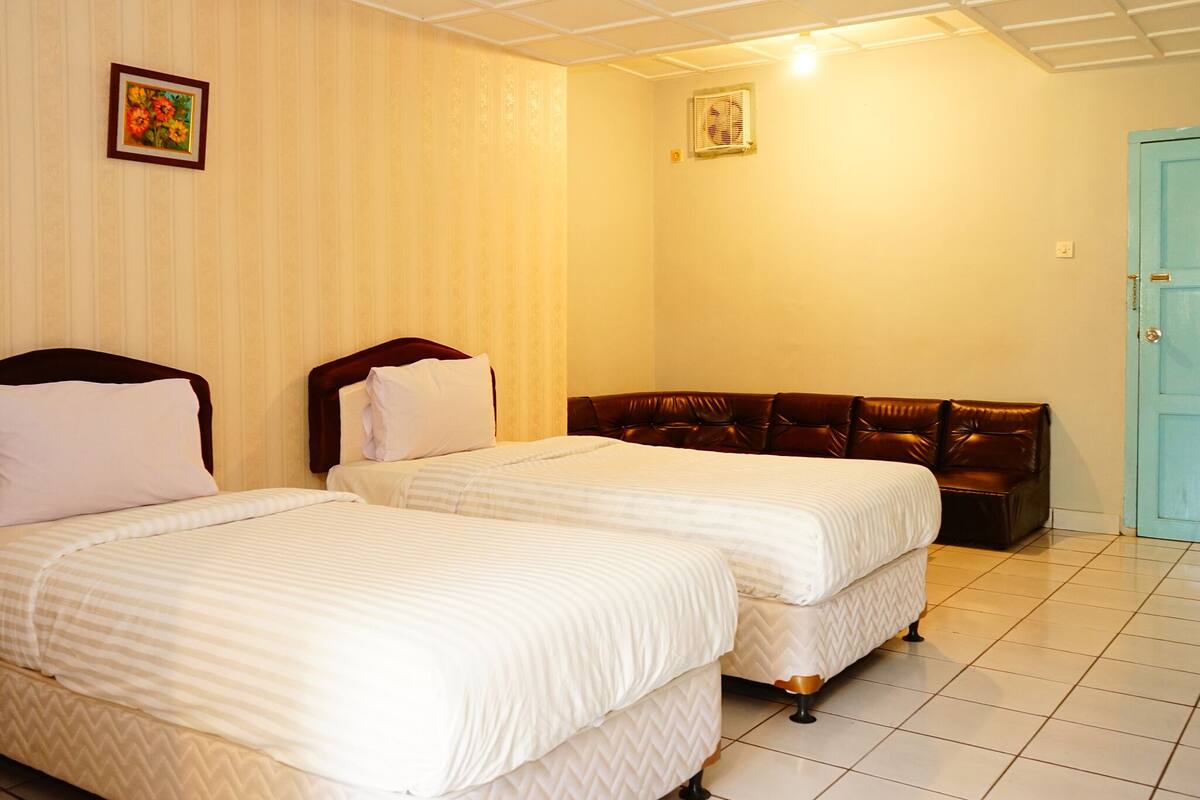 A hotel room with two beds, a brown leather sofa, a blue door, and a ceiling fan.