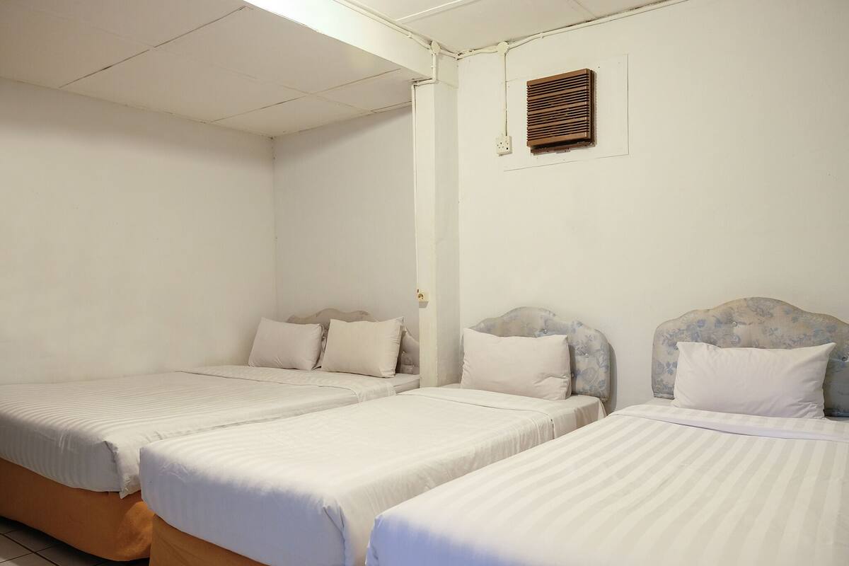 A hotel room with three single beds, each with a headboard and white bedding.