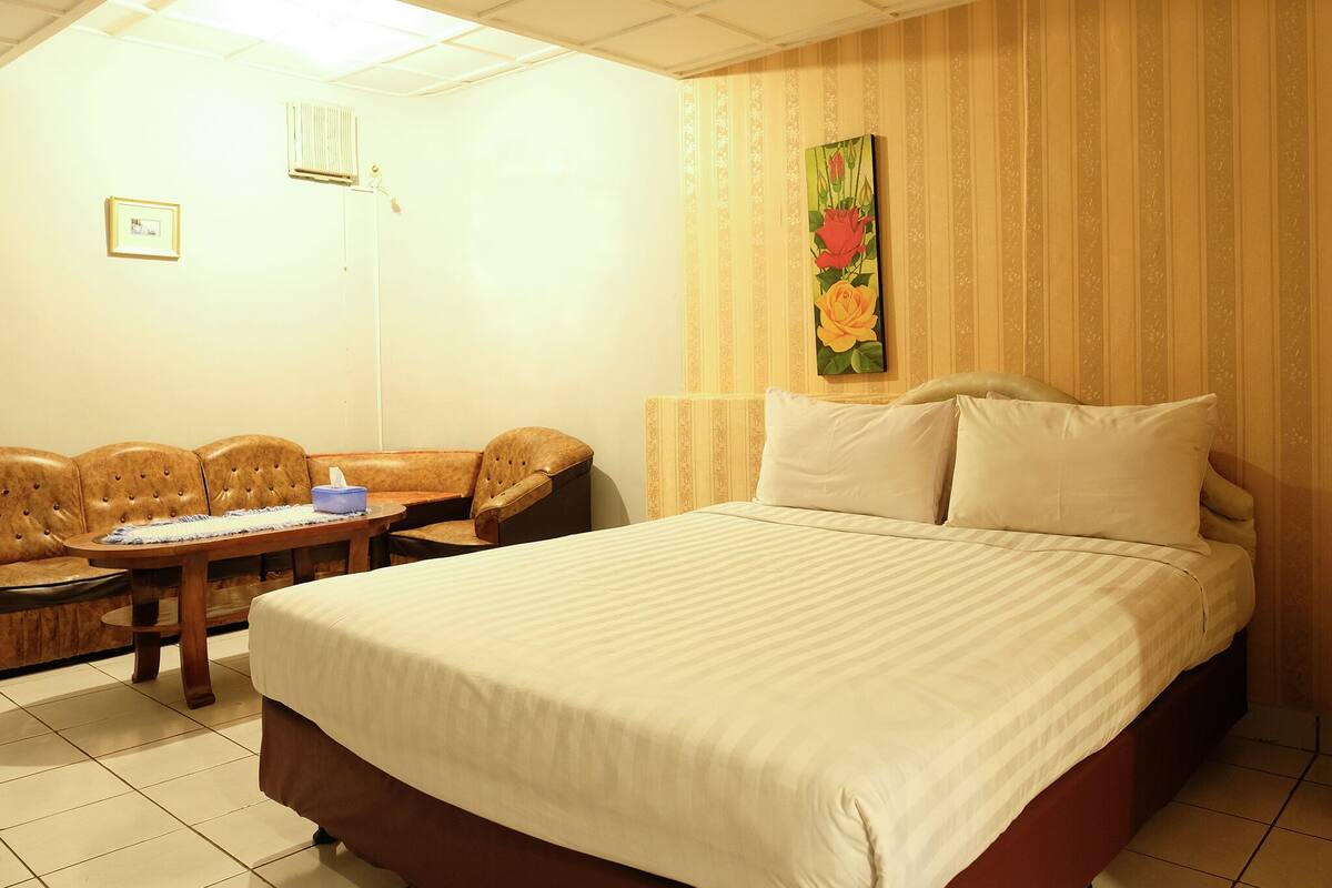 A hotel room with a large bed, a sofa, a small table, and a painting on the wall.