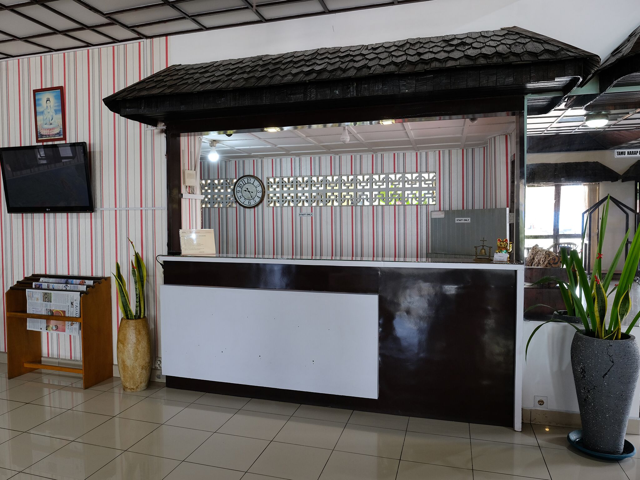 A reception desk with a clock, striped wallpaper, and a television mounted on the wall.