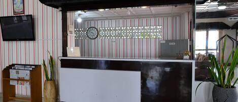 A reception desk with a clock, striped wallpaper, and a television mounted on the wall.