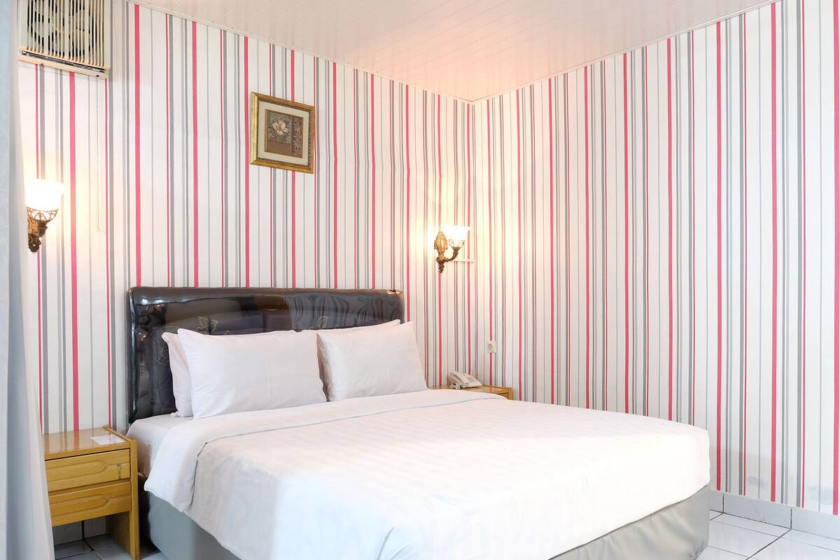 A neatly made bed with white linens, a wooden nightstand with a lamp, and a wall with vertical striped wallpaper.
