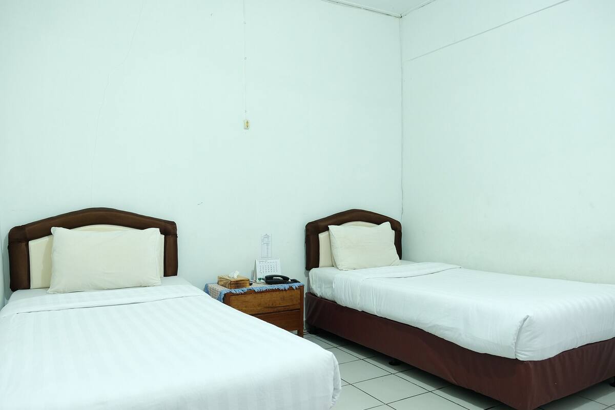 A twin room with two beds, a nightstand with a phone and calendar, and a wall-mounted light fixture.
