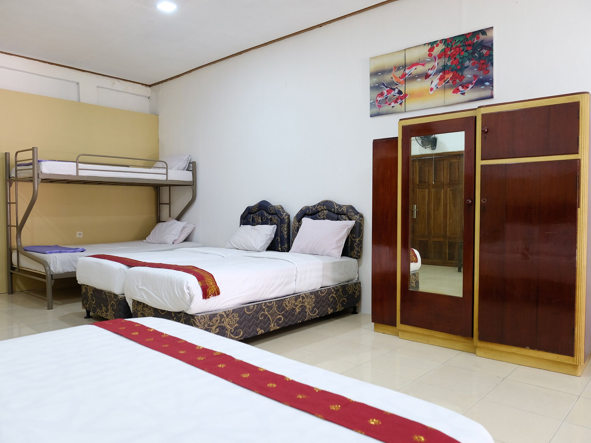 A room with a bunk bed, a single bed with patterned bedding, a wardrobe, and a painting on the wall.