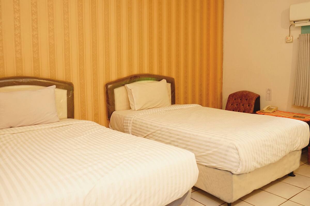 A hotel room with two single beds, a wooden chair, a telephone, and a wall-mounted air conditioner.