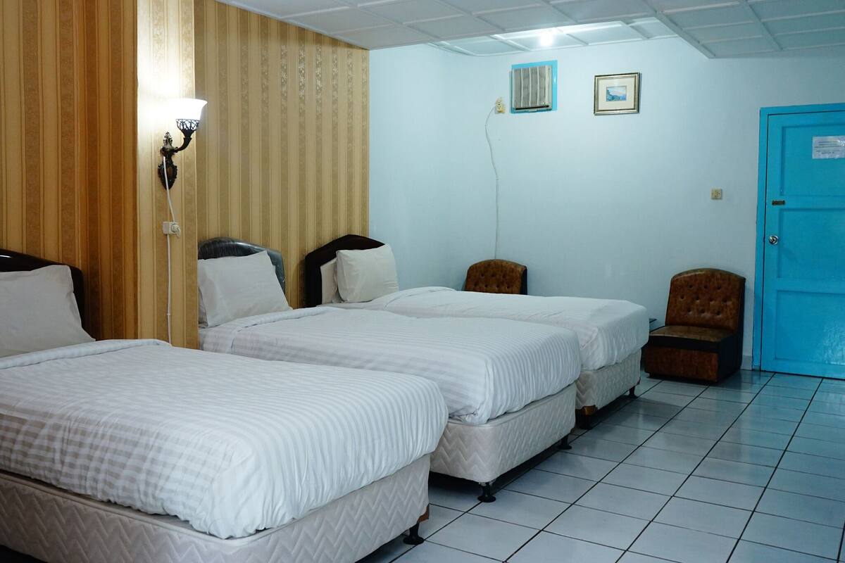 A hotel room with two beds, a wooden panel wall, a blue door, and a tiled floor.