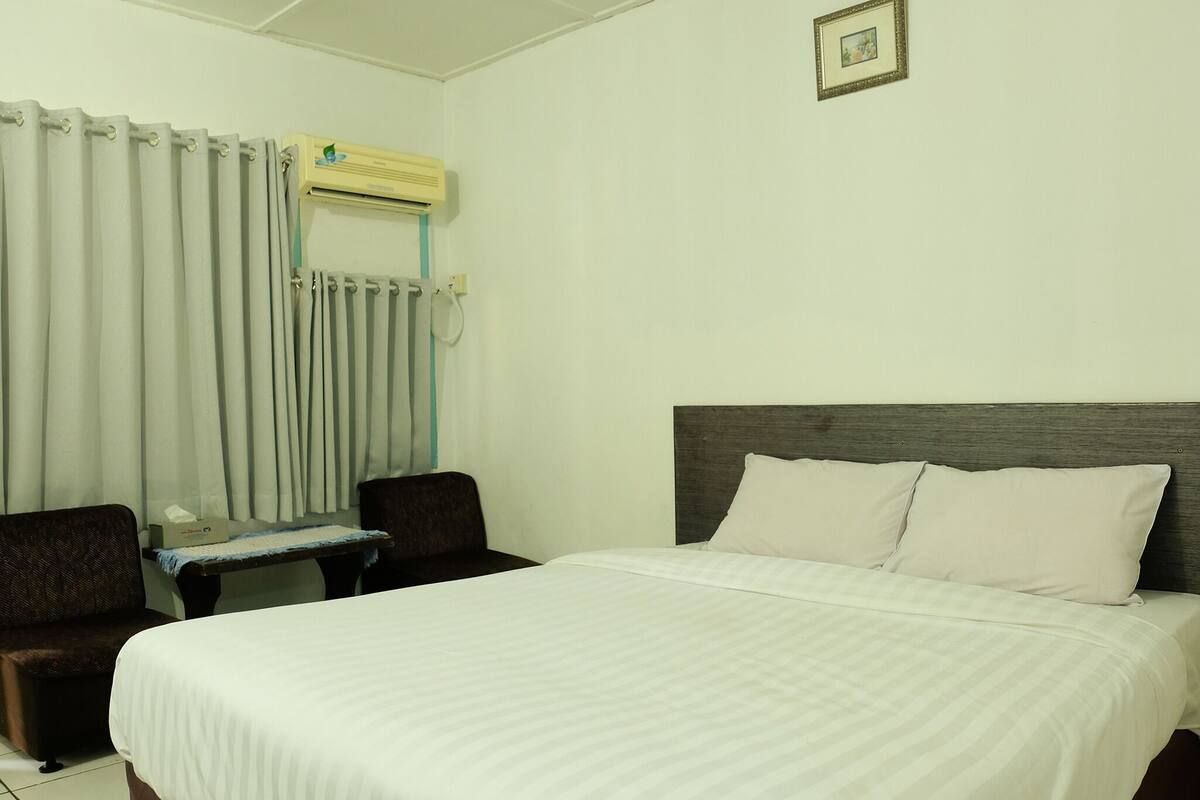 A hotel room with a bed, a desk, a chair, and a window with curtains.