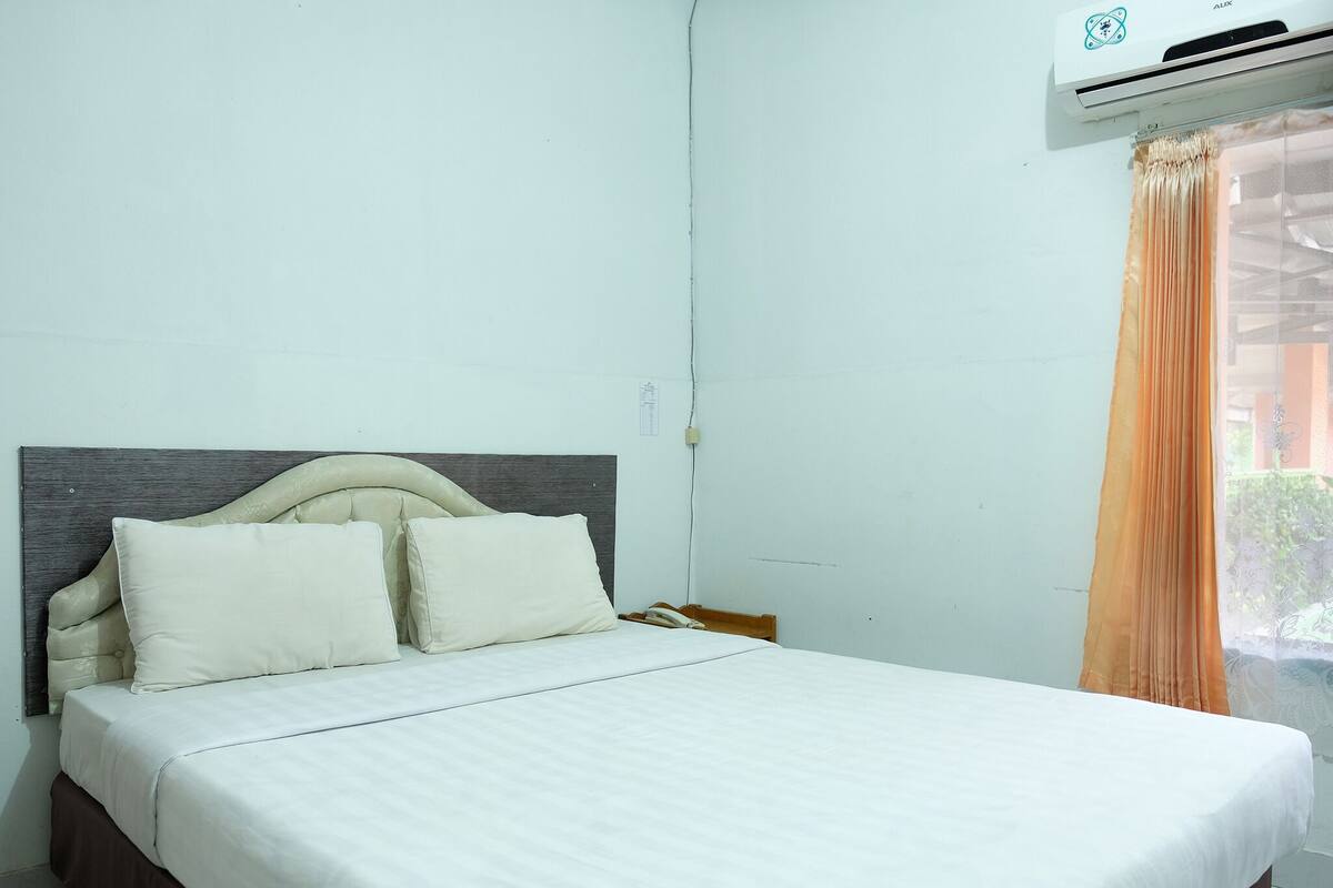 A neatly made bed with a headboard, a white wall, and an air conditioning unit above it.