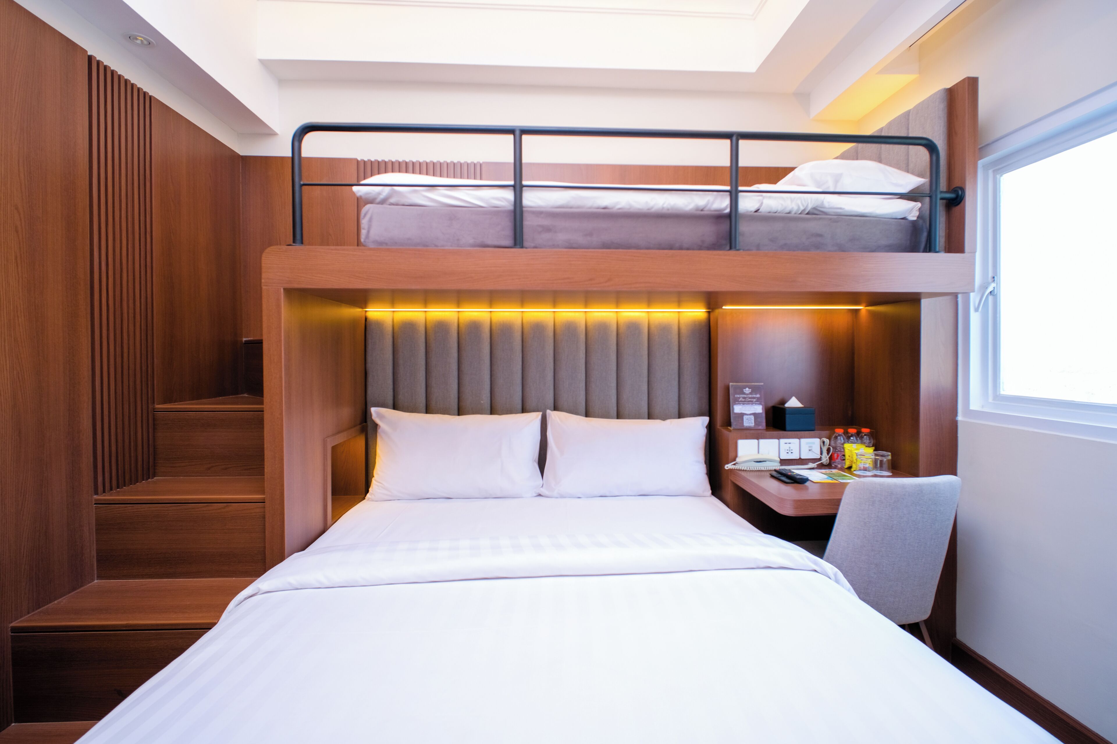 A bunk bed with a desk and chair, wooden paneling, and a window.