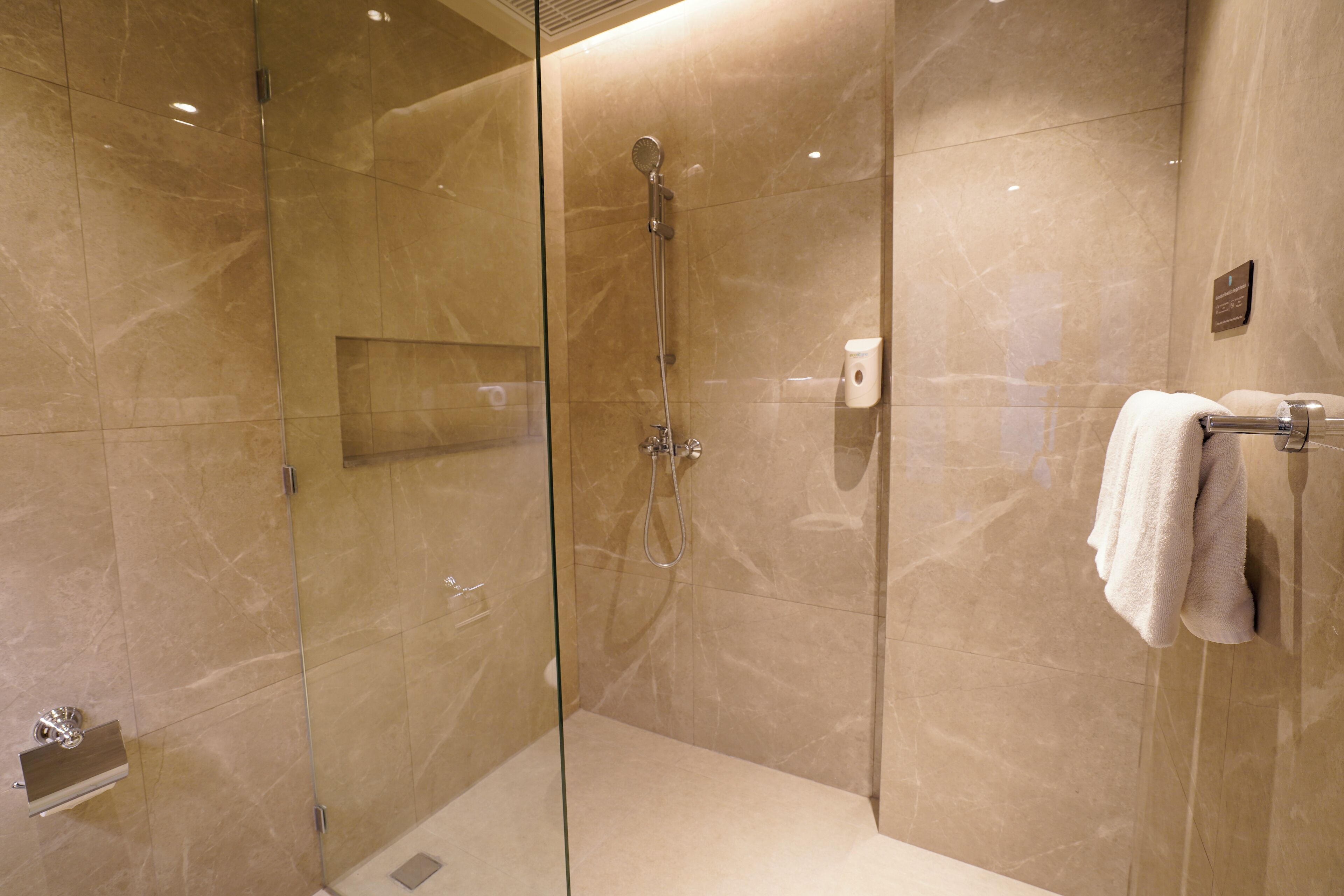 Un baño moderno con ducha de vidrio, paredes de mármol y un perchero para toallas.