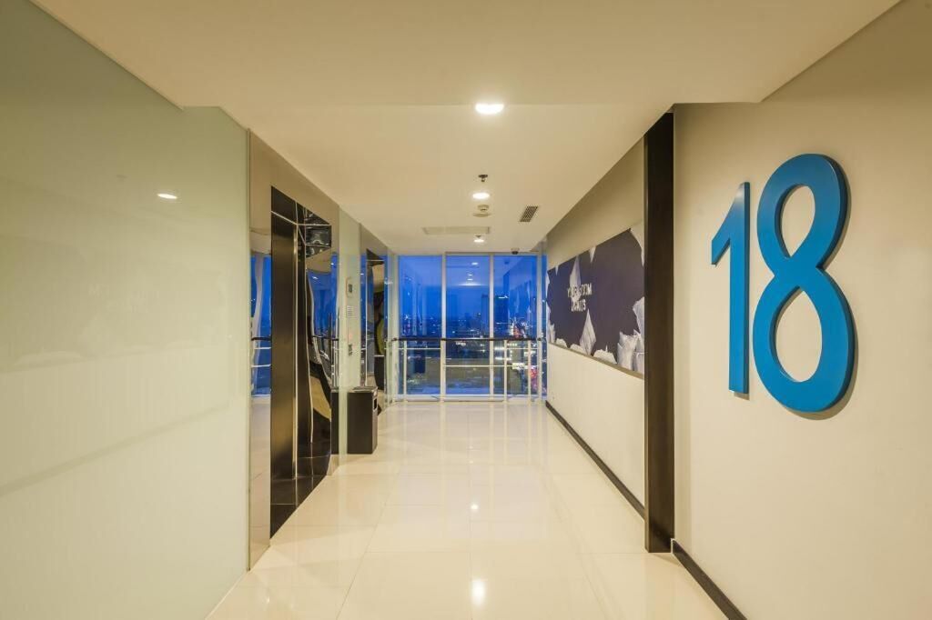 Un pasillo moderno de hotel con un cartel grande con el número 18, puertas de cristal que dan a un balcón y un suelo de baldosas impecable.