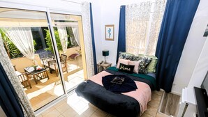 Quarto com cama, mesa de cabeceira, luminária, porta de vidro deslizante para um pátio e pequena mesa com cadeiras.