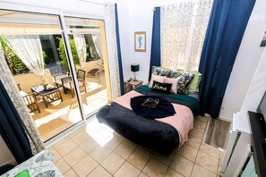 A bedroom with a bed, a nightstand, a lamp, a sliding glass door to a patio, and a small table with chairs.