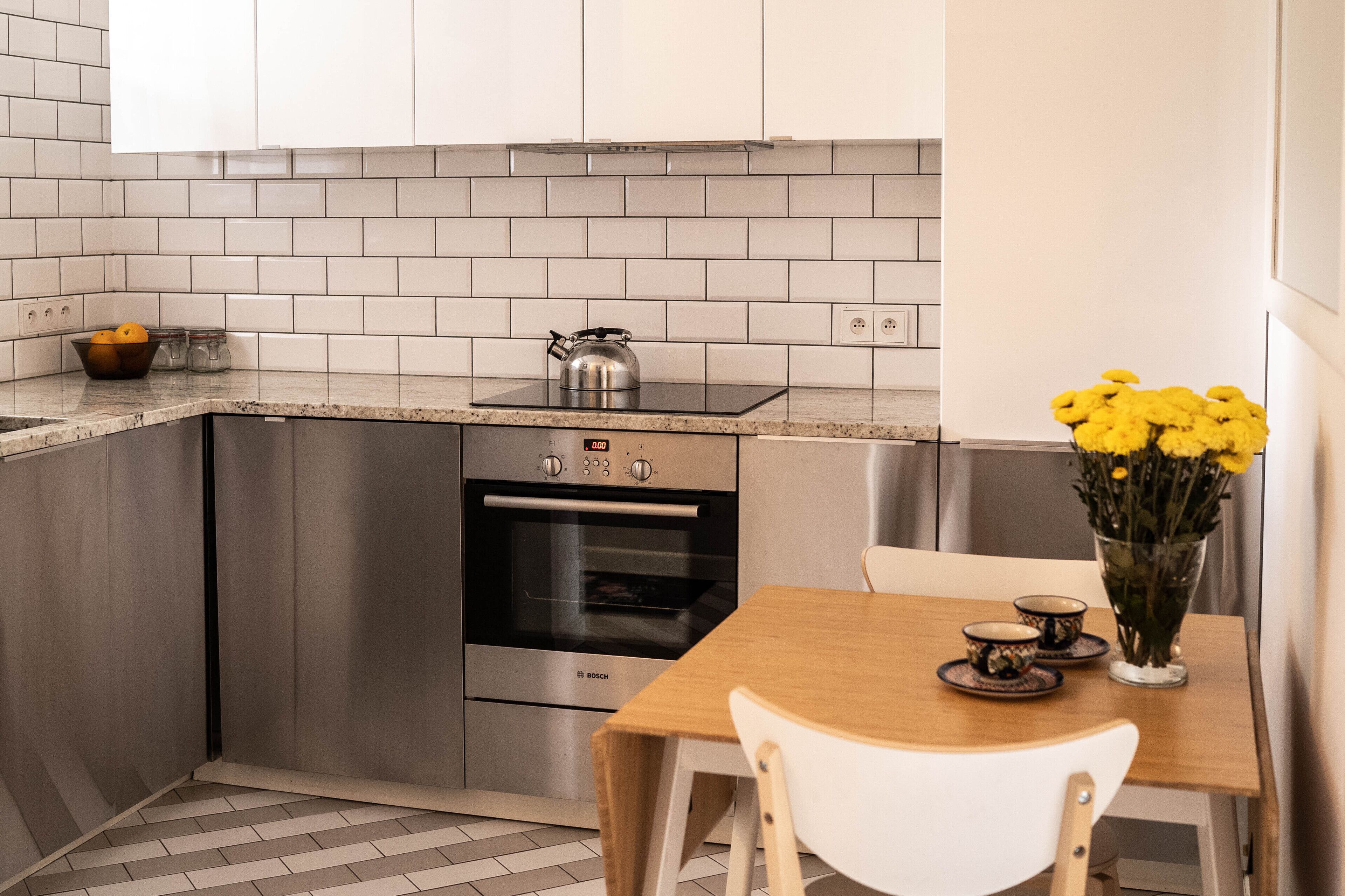 A modern kitchen with stainless steel appliances, a wooden table, and a vase of yellow flowers.