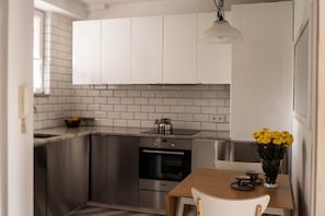 A modern kitchen with white cabinets, a stainless steel oven, a kettle, and a vase with yellow flowers on the table. - P&O Apartments Corazziego Metro Ratusz (Warsaw)