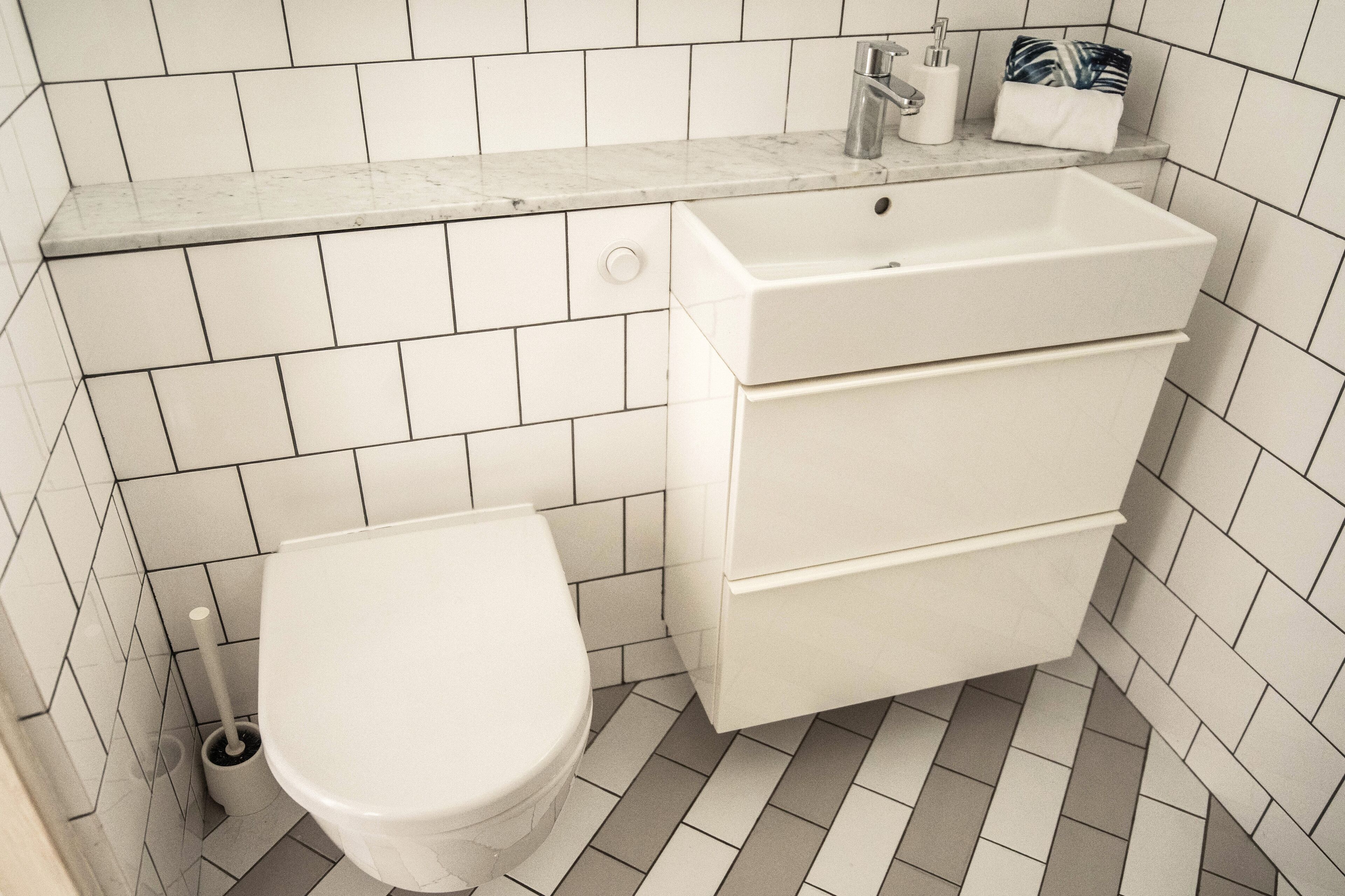 A bathroom with a toilet, sink, and storage cabinet.