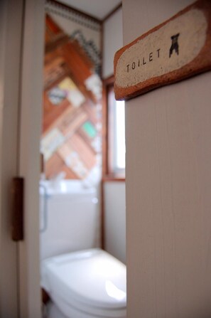 A small, compact bathroom with a white toilet and a wooden sign indicating the toilet's location. - Nikko Guesthouse Sumica - Hostel (Nikko)
