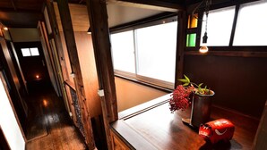 A narrow wooden corridor with a window on the right, a small table with a potted plant, and a red object on the table. - Nikko Guesthouse Sumica - Hostel (Nikko)