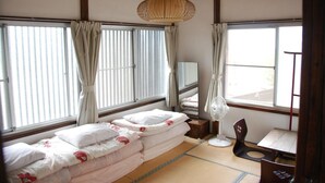 A traditional Japanese room with tatami flooring, a low bed with a canopy, a desk with a chair, and a large window with curtains. - Nikko Guesthouse Sumica - Hostel (Nikko)