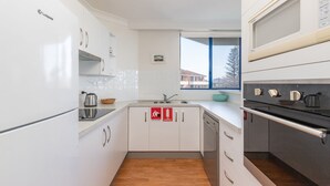 A modern kitchen with white cabinets, stainless steel appliances, and a window with a view of buildings. - Enjoy wonderful water views from Heritage 303 (Tuncurry)