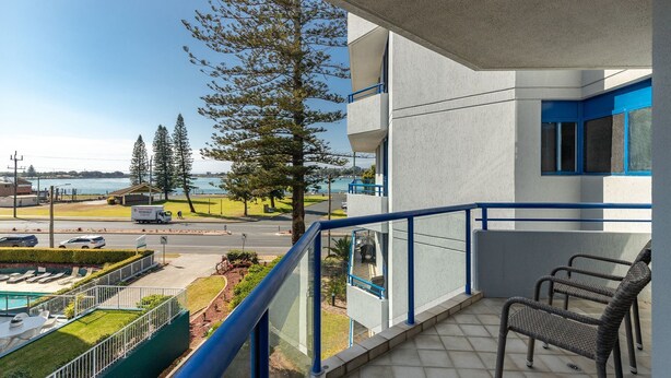 A balcony with a view of a body of water, a parking area, and a building with blue accents. - Enjoy wonderful water views from Heritage 303 (Tuncurry)