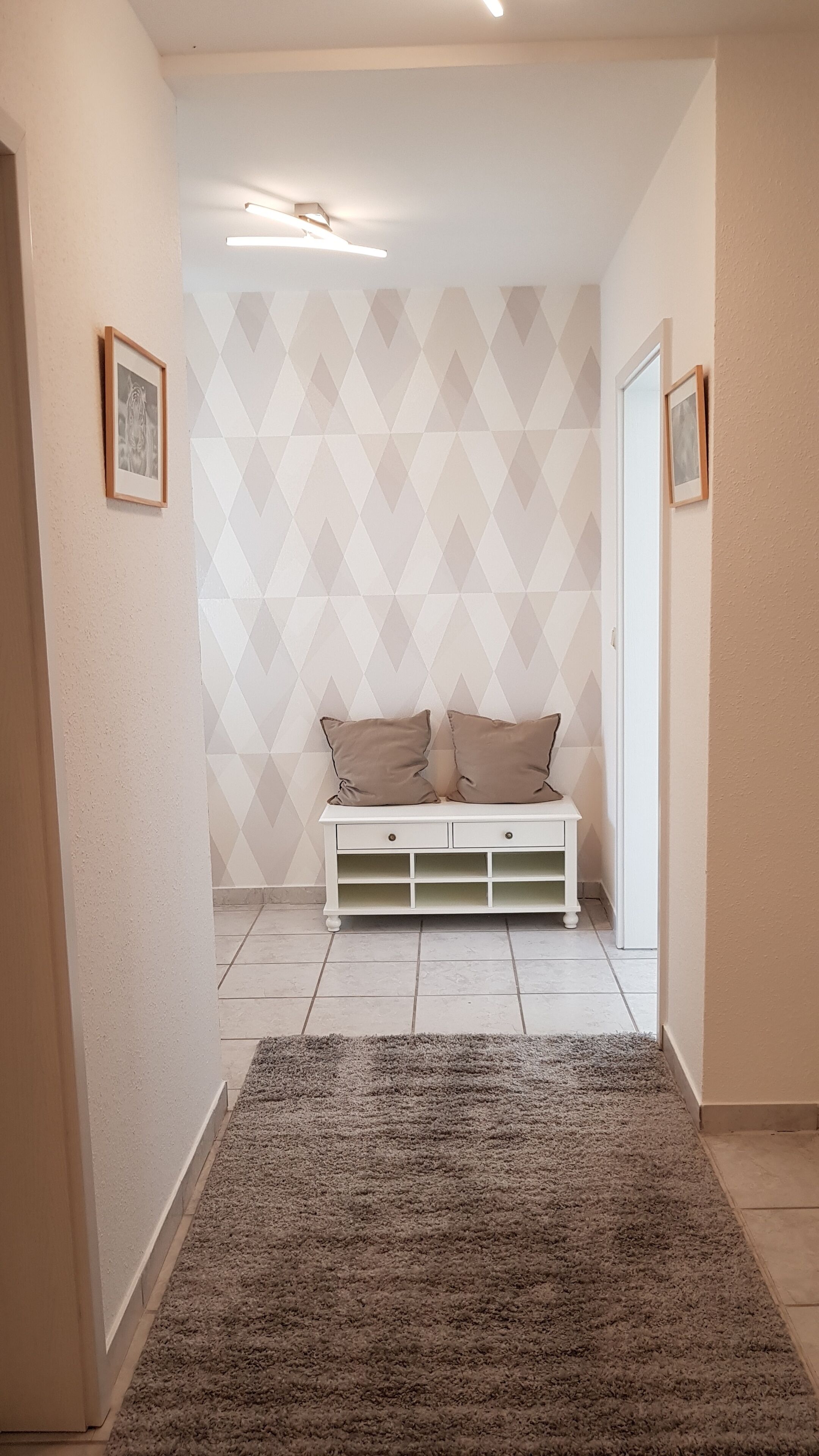 Ein Flur mit einer weißen Bank, geometrischem Wandpapier und einem grauen Teppich.