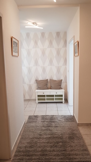 A hallway with a white bench, geometric patterned wallpaper, and a grey carpet.