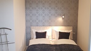 Ein Schlafzimmer mit einem Bett, einer Wand mit Muster, einer stehenden Lampe und einem grauen Teppich.