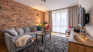 A living room with a brick wall, a grey sofa, a coffee table, and a TV on a wooden stand. - P&O Apartments Okecie 5 (Warsaw)
