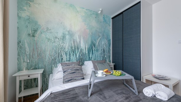 A modern bedroom with a large bed, white nightstands, a bedside table with a tray, and a large abstract wall mural. - P&O Apartments Okecie 5 (Warsaw)