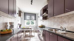 A modern kitchen with dark cabinets, a stainless steel sink, and a dining area with a table and chairs. - P&O Apartments Okecie 5 (Warsaw)