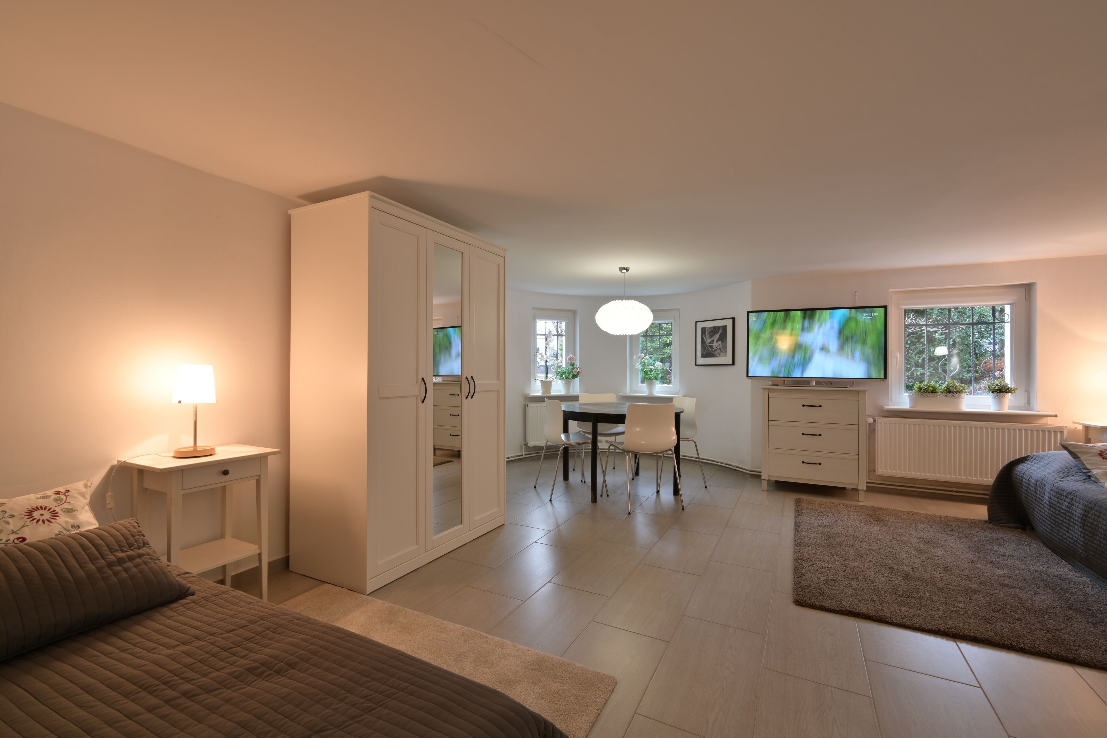 Ein modernes Schlafzimmer mit Bett, Nachttisch und Fernseher im Hintergrund.