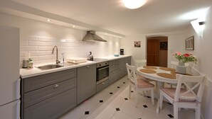 Een moderne keuken met grijze kastjes, een roestvrijstalen spoelbak en een inbouwoven. Er is een eethoek met een ronde tafel en witte stoelen.