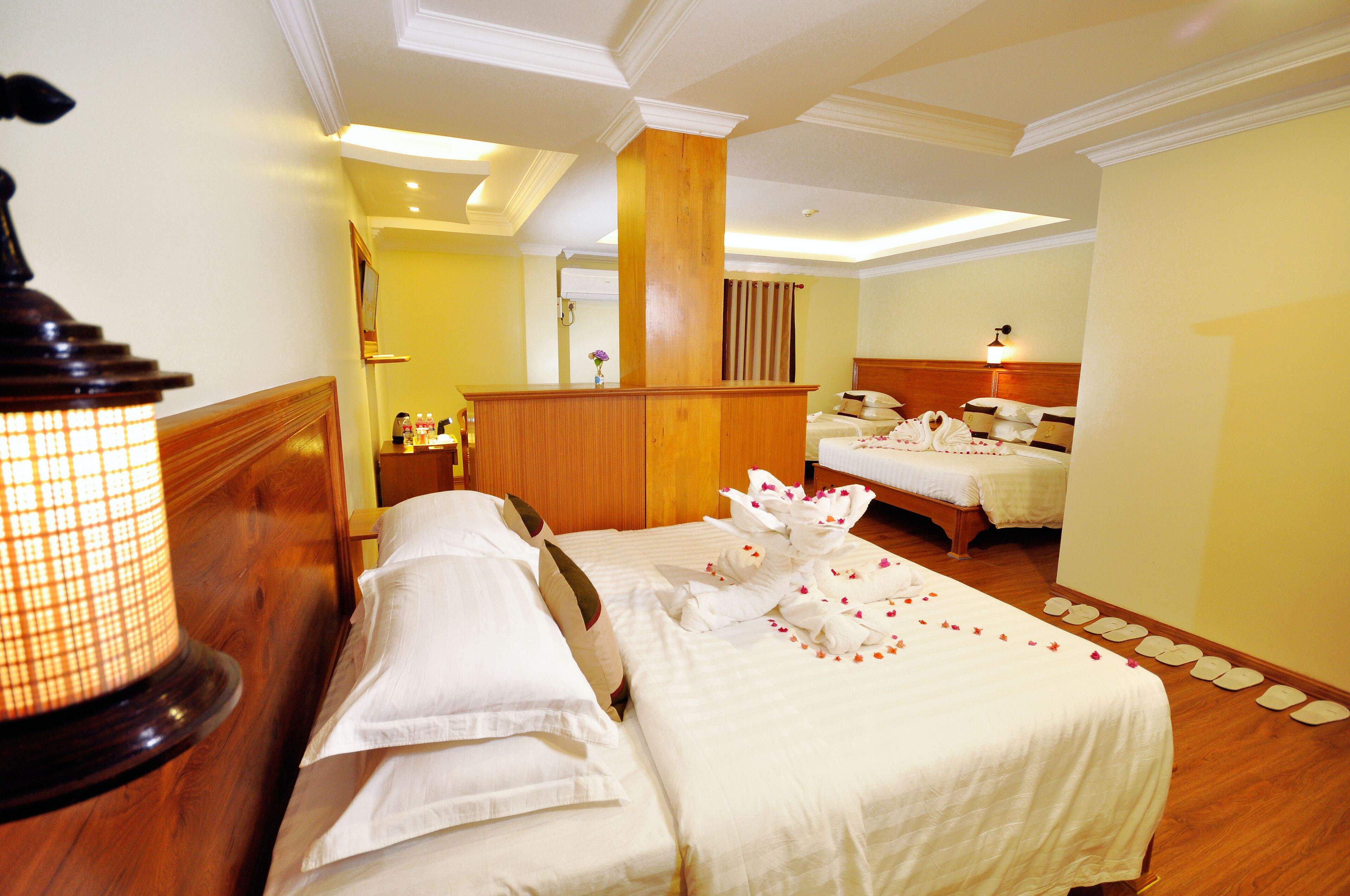 A hotel room with two beds, a wooden headboard, a nightstand, a lamp, and a mirror.