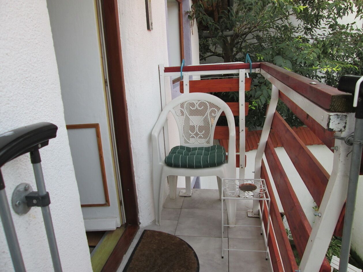 A small outdoor balcony with a white chair, a red and white railing, and a metal table.