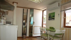 A compact kitchen with a dining area, a small table, and chairs. There is a window with blinds, a radiator, and a door leading to another room. - STUDIO GREEN   near city center, free parking, wifi, at banks of river Sava (Zagreb)